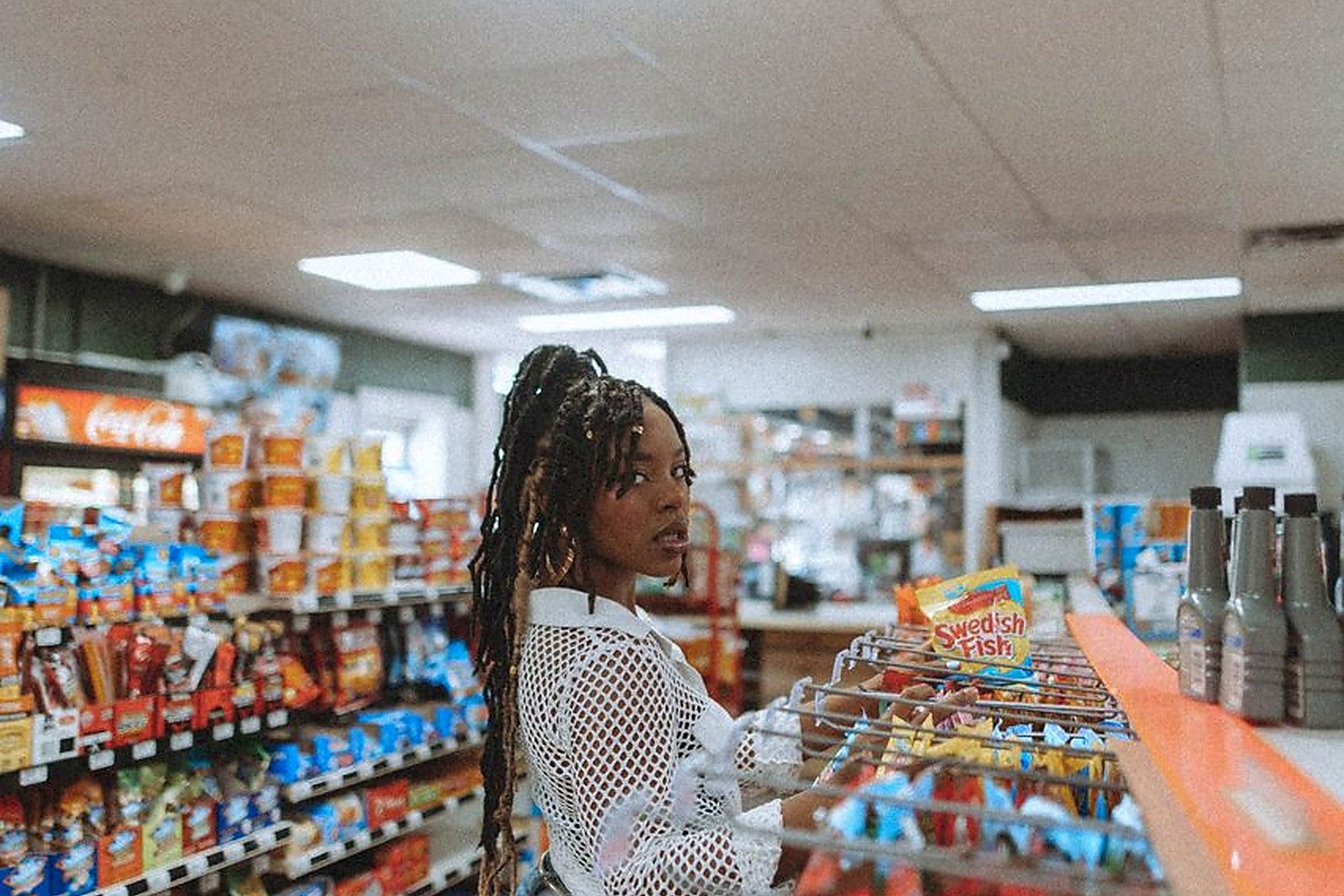 Free African American woman standing in a grocery store aisle, picking snacks. Indoor retail scene. Stock Photo